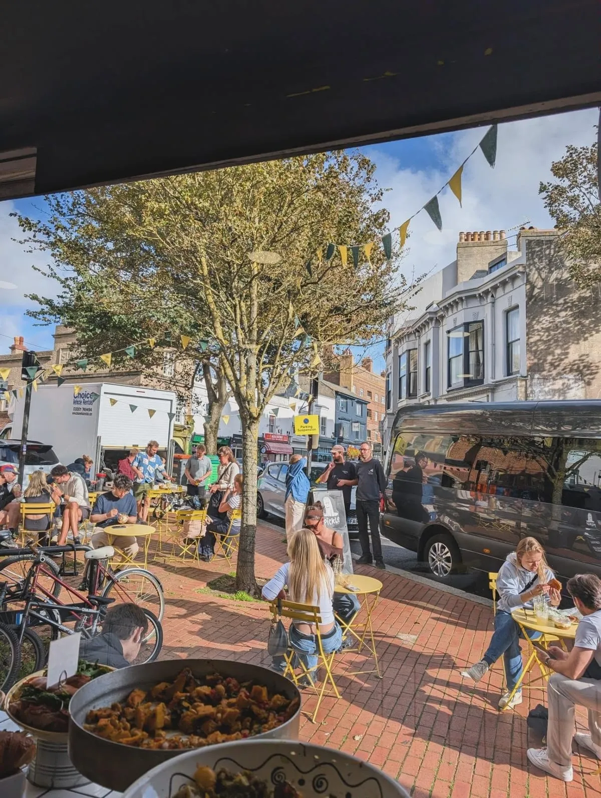 People sitting at yellow tables in the pickle square outside The Pickle, Kemptown
